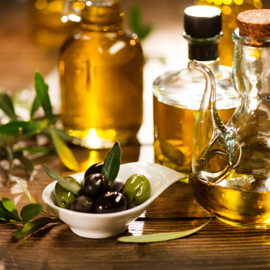 El aceite de oliva no puede faltar en ninguna comida italiana. Fíjese en el aceite de oliva italiano de alta calidad de la foto. Está embotellado y colocado sobre una mesa junto a las aceitunas en un pequeño cuenco blanco.