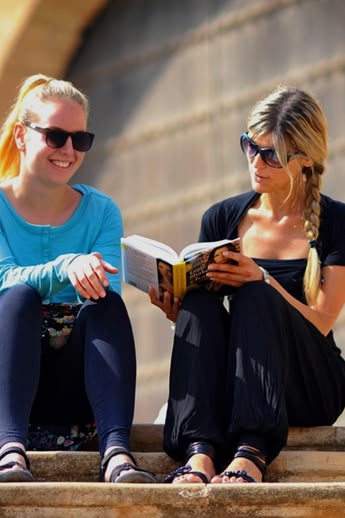 Two Sprachcaffe students sitting on steps in Rabat, Morocco, reading and chatting in front of traditional architecture.