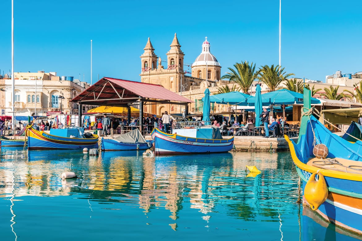 Colourful fishing boats and waterfront cafés at Marsaxlokk market in Malta.