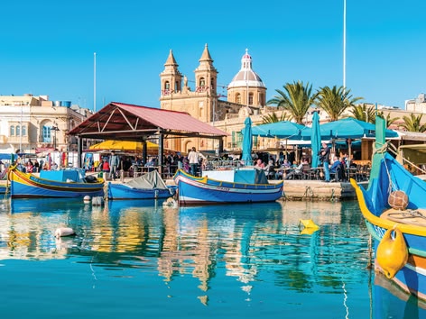 Colourful fishing boats and waterfront cafés at Marsaxlokk market in Malta.