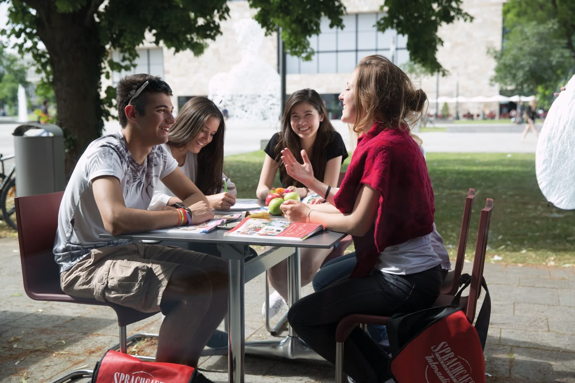 Sprachcaffe students studying together at an outdoor table in a sunny park setting.