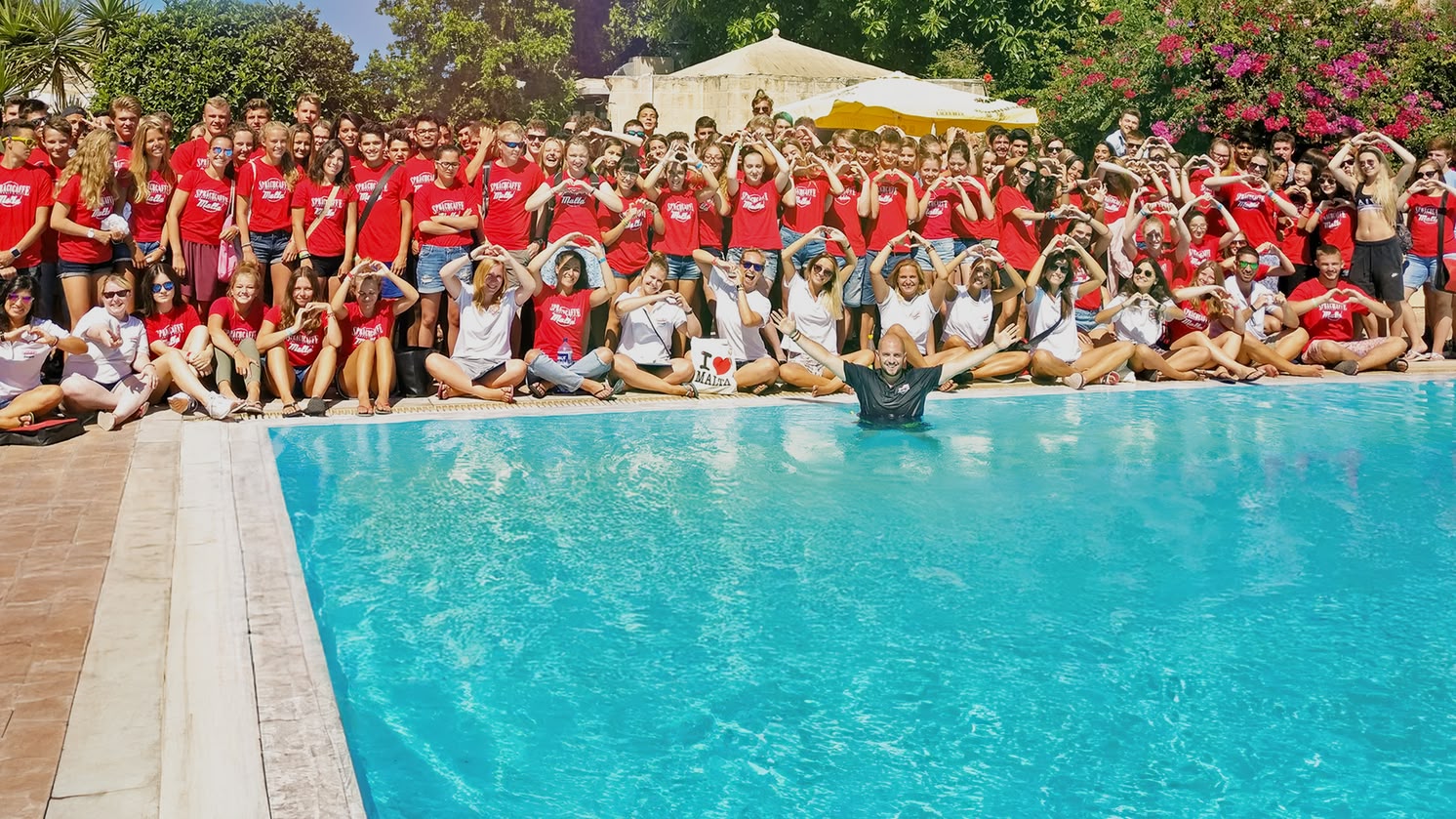 Grande grupo de alunos juniores da Sprachcaffe em Malta posando à beira da piscina, muitos formando corações com as mãos.