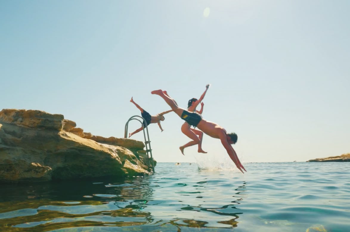Group of teens jumping into the sea from rocks on a sunny day.