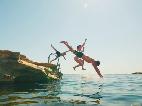 Group of teens jumping into the sea from rocks on a sunny day.