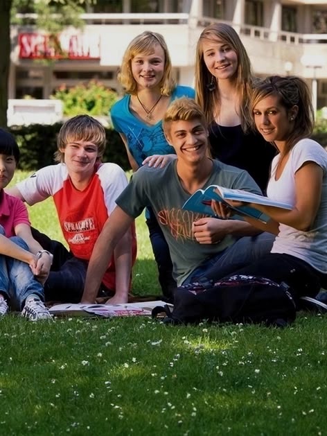 Frankfurt, Almanya'da çimlerin üzerinde oturan bir grup Sprachcaffe genç öğrencisi, gülümsüyor ve güneşli bir günün tadını çıkarıyor.
