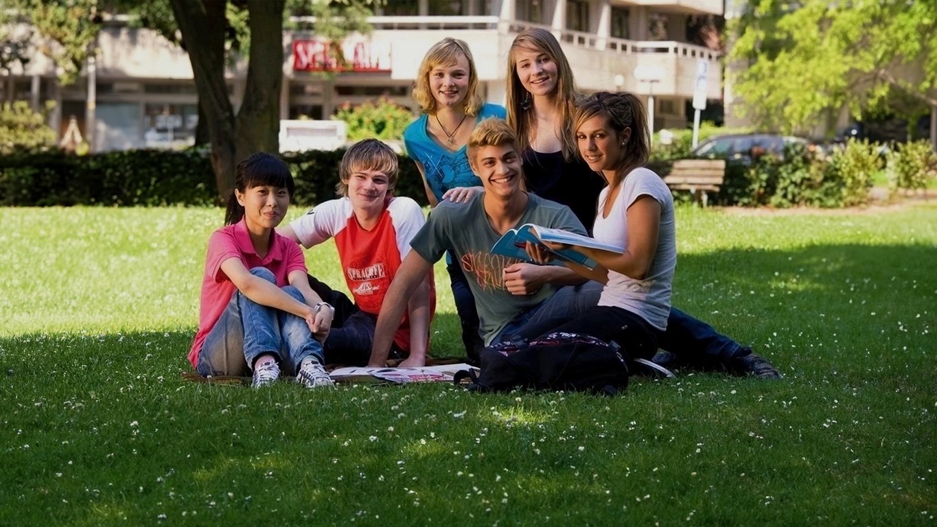Group of Sprachcaffe junior students sitting on the grass in Frankfurt, Germany, smiling and enjoying a sunny day.