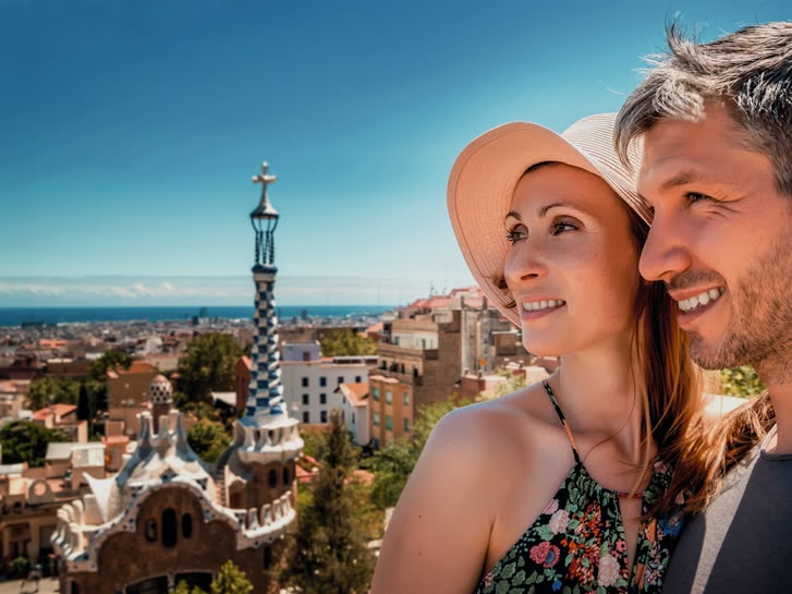Smiling couple enjoying the view from Park Güell in Barcelona, Spain, with the city and sea in the background.