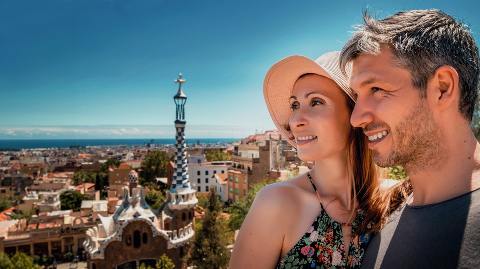 Smiling couple enjoying the view from Park Güell in Barcelona, Spain, with the city and sea in the background.
