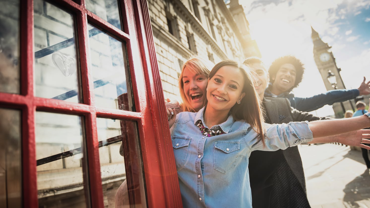 Garota sorridente posando ao lado de uma cabine telefônica vermelha em Londres, com o Big Ben visível ao fundo.