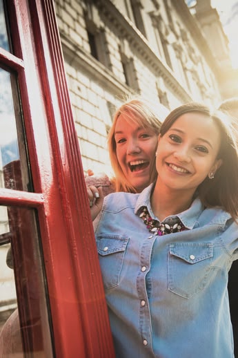 Smiling girl posing by a red phone booth in London with Big Ben visible in the background.