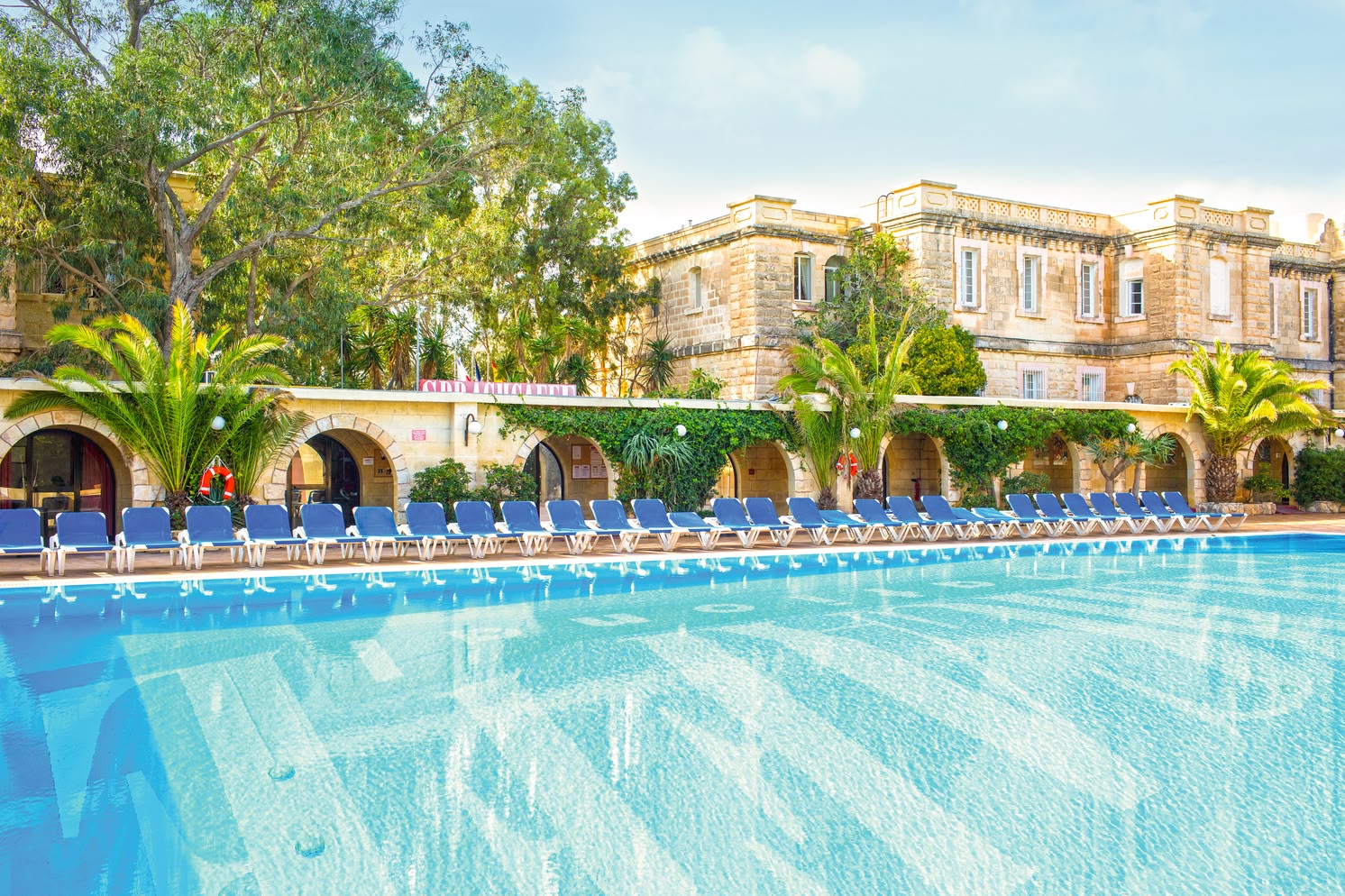 Large outdoor pool surrounded by lounge chairs and historic buildings at the Sprachcaffe campus in St. Julian’s, Malta.