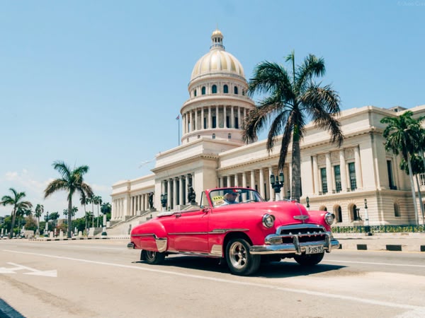 Klasyczny samochód przejeżdża przed budynkiem Kapitolu w Hawanie, Kuba, łącząc historyczny urok z tropikalnym klimatem miasta.