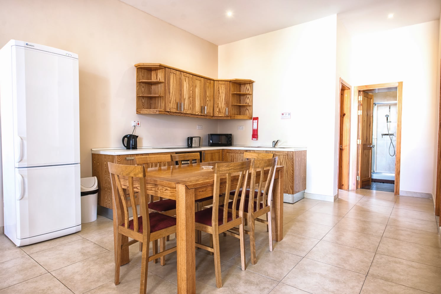 Simple student kitchen and dining area at Sprachcaffe Malta, featuring wooden furniture and basic appliances.