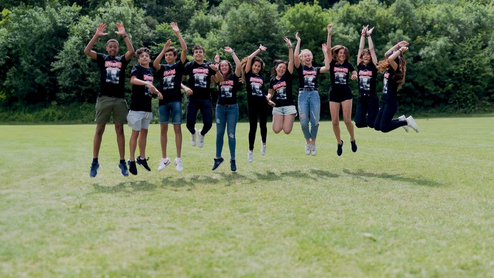 Sprachcaffe students in England jumping mid-air on a green field, wearing matching shirts and enjoying the outdoors.