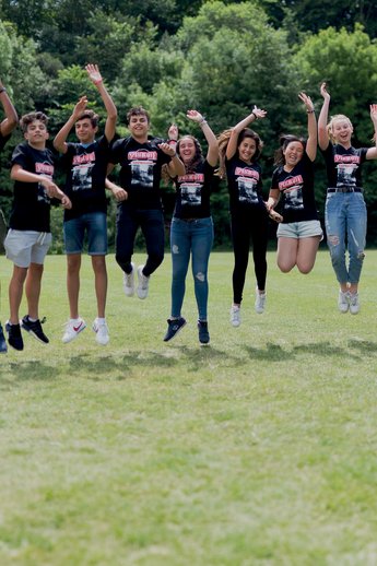 Sprachcaffe students in England jumping mid-air on a green field, wearing matching shirts and enjoying the outdoors.