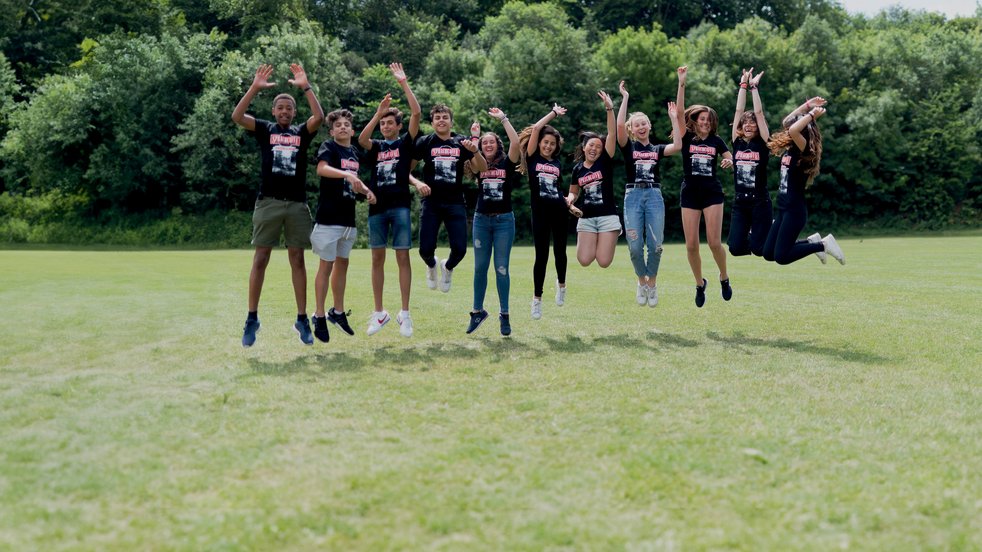 Sprachcaffe students in England jumping mid-air on a green field, wearing matching shirts and enjoying the outdoors.