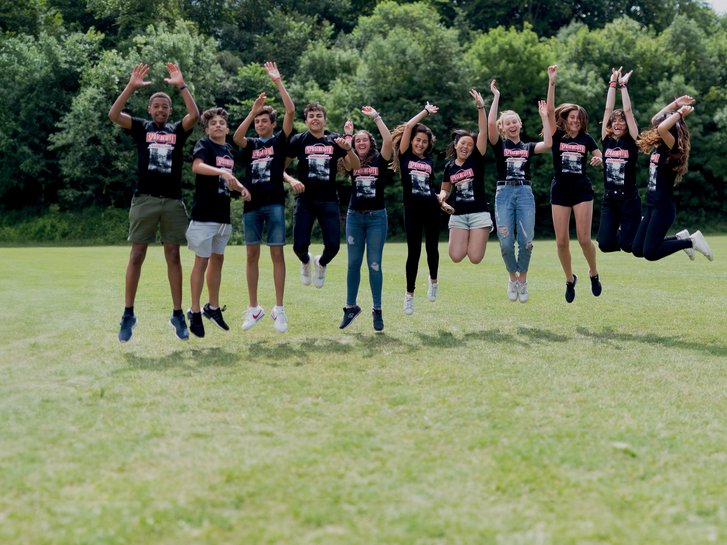 Sprachcaffe students in England jumping mid-air on a green field, wearing matching shirts and enjoying the outdoors.