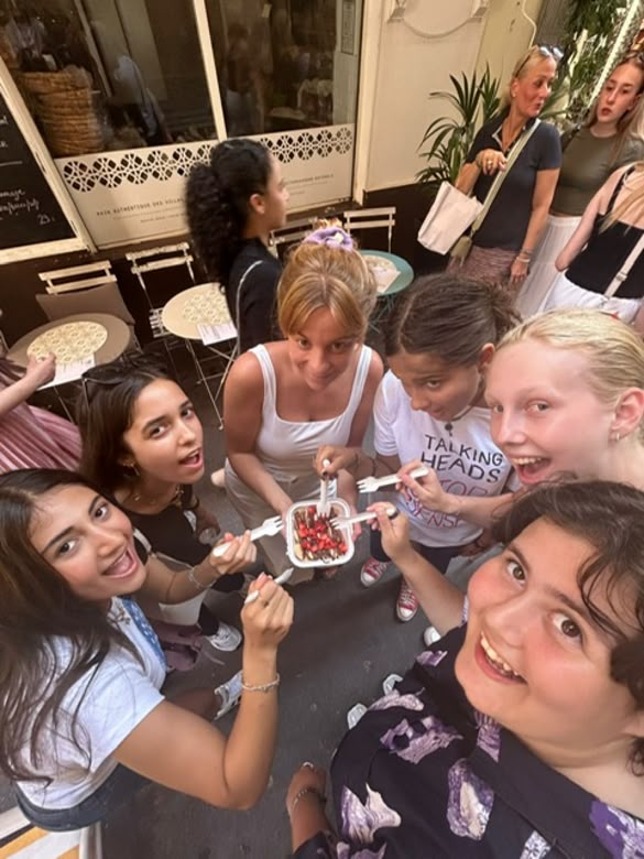 Group of smiling girls sharing a dessert on a street in Nice, France, in front of a café.