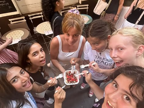 Group of smiling girls sharing a dessert on a street in Nice, France, in front of a café.