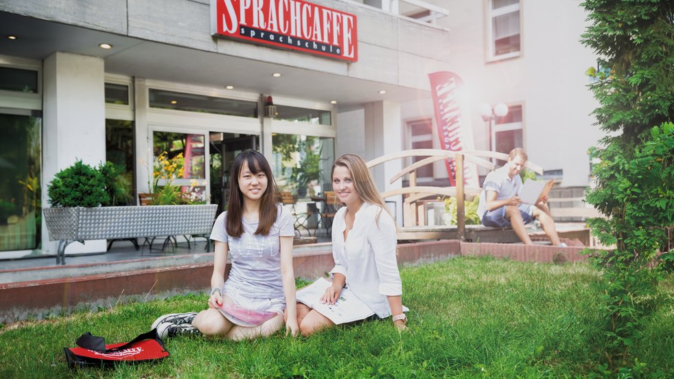 Two young women sitting on the grass in front of the Sprachcaffe language school in Frankfurt, Germany.