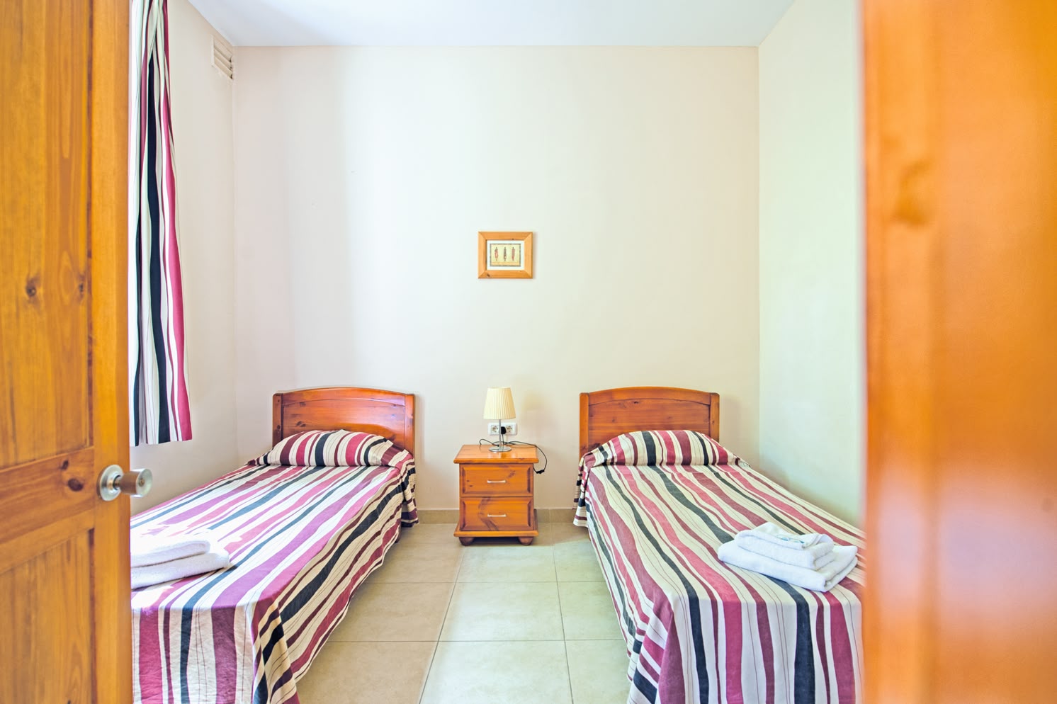 Basic student twin room at Sprachcaffe Malta with striped bedding, wooden furniture, and tiled floors.
