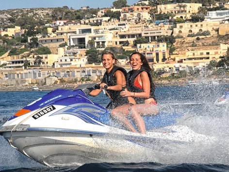 Two young women smiling while riding a jet ski along Malta's coast.