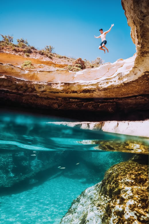 Teen jumping into a natural pool from a rocky cliff.