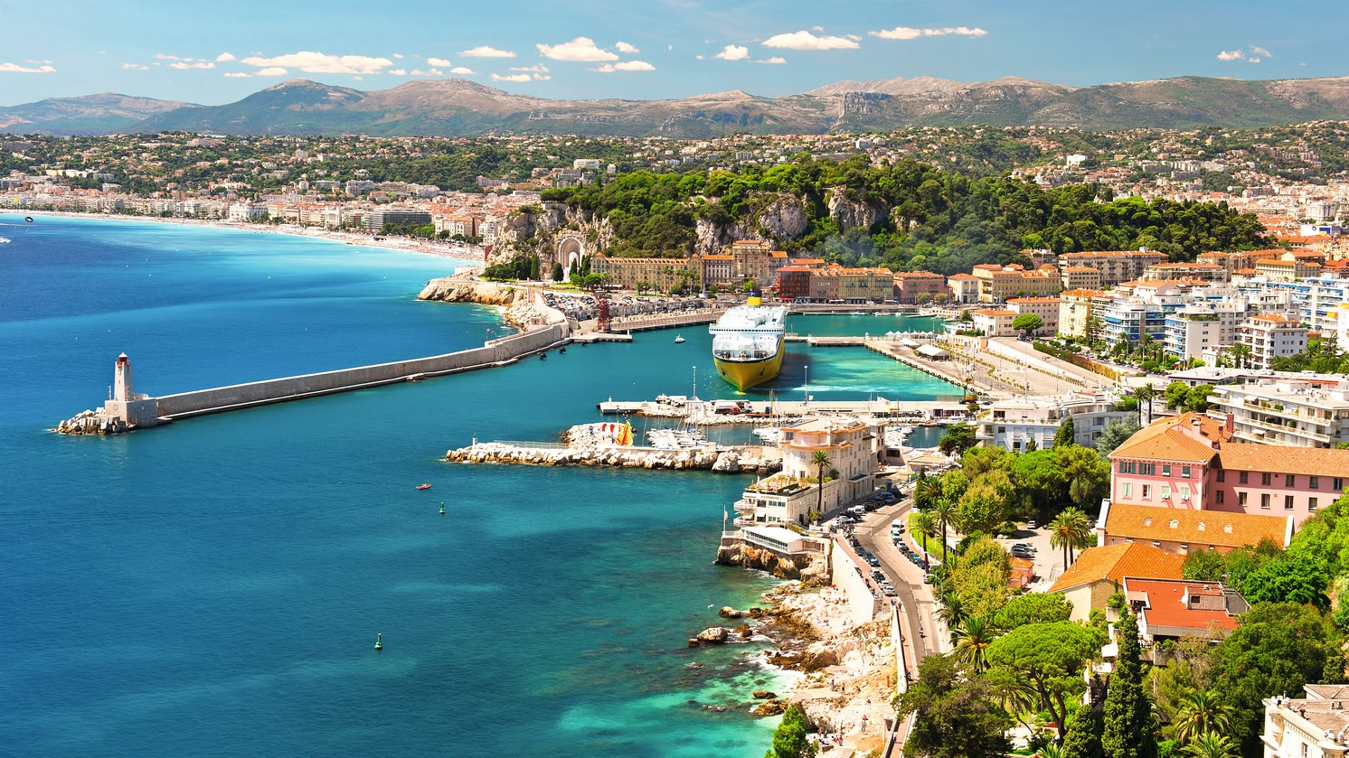 **ALT:** Widok z lotu ptaka na malowniczą Niceę, Francja, z turkusowymi wodami Morza Śródziemnego, portem i zabudową miejską otoczoną zielenią.