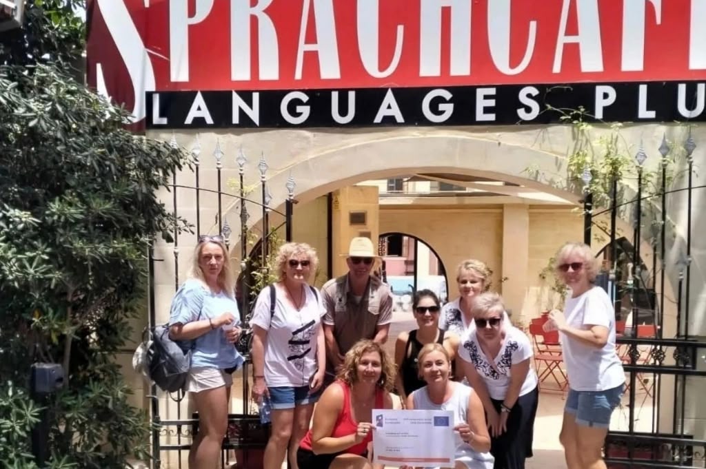 Grupa studentów Sprachcaffe pozuje pod szyldem szkoły, trzymając certyfikat ukończenia kursu