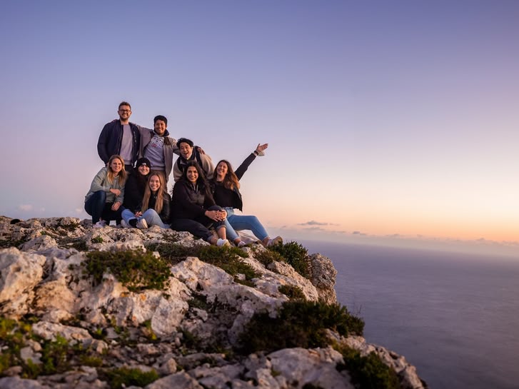 Group of young adults on a rocky cliff in Malta at sunset, overlooking the sea and enjoying the view.
