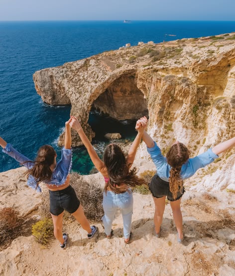 Three girls raising arms on cliffs overlooking the Blue Grotto.