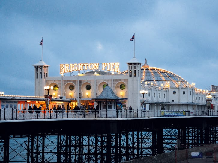 Brighton Pier o zmierzchu, widok na oświetlone molo z charakterystyczną kopułą, otoczone niebieskim niebem i morzem