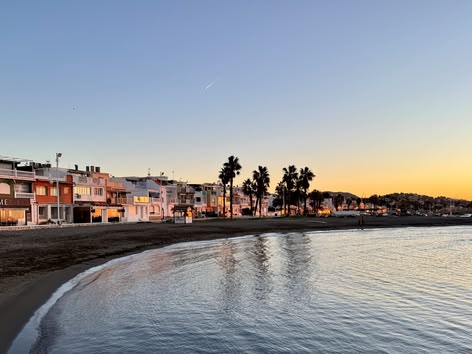 Sunset view of Pedregalejo beach in Málaga with palm trees and seafront houses.
