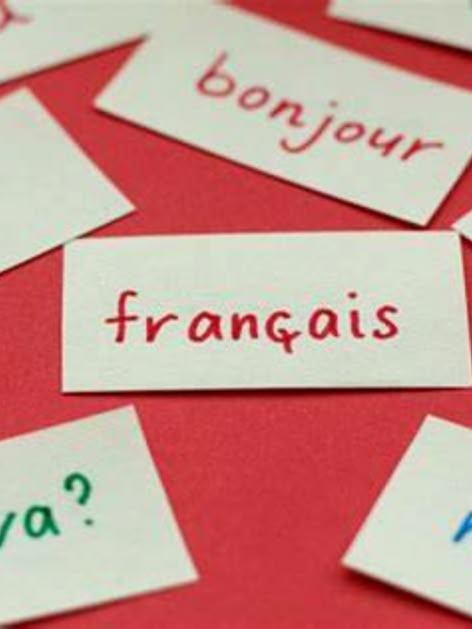 **ALT:** Kartki z francuskimi słowami i zwrotami, takimi jak "français," "bonjour," "le," "ça va?," i "merci," rozłożone na czerwonym tle.