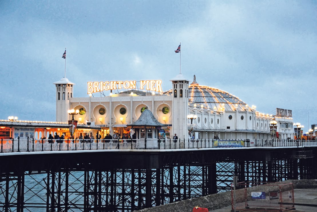 Jasno oświetlone Brighton Palace Pier o zmierzchu, tętniące życiem molo z licznymi atrakcjami, restauracjami i arkadami, stanowiące obowiązkowy punkt na mapie Brighton
