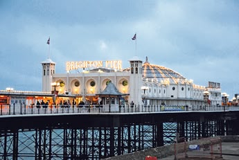 Jasno oświetlone Brighton Palace Pier o zmierzchu, tętniące życiem molo z licznymi atrakcjami, restauracjami i arkadami, stanowiące obowiązkowy punkt na mapie Brighton